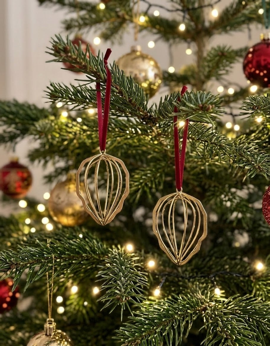 Pair of gold metal pinecone Christmas ornaments hanging with dark red ribbons on illuminated pine branches.