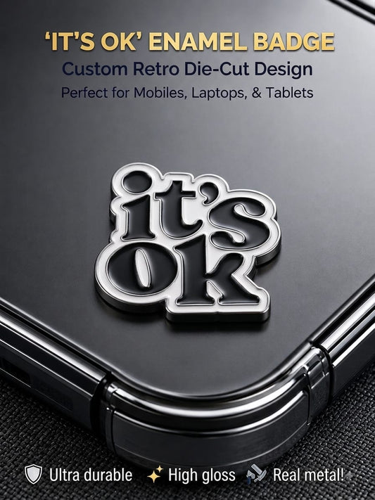 Black and silver retro die-cut "It's OK" metal enamel badge sticker applied to the back of a smartphone.