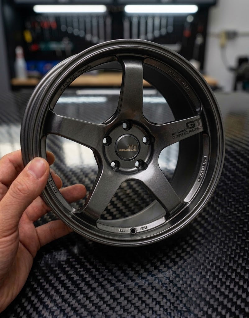 Hand holding a 10cm gunmetal grey 5-spoke diecast aluminum miniature wheel showing realistic scale and finish.