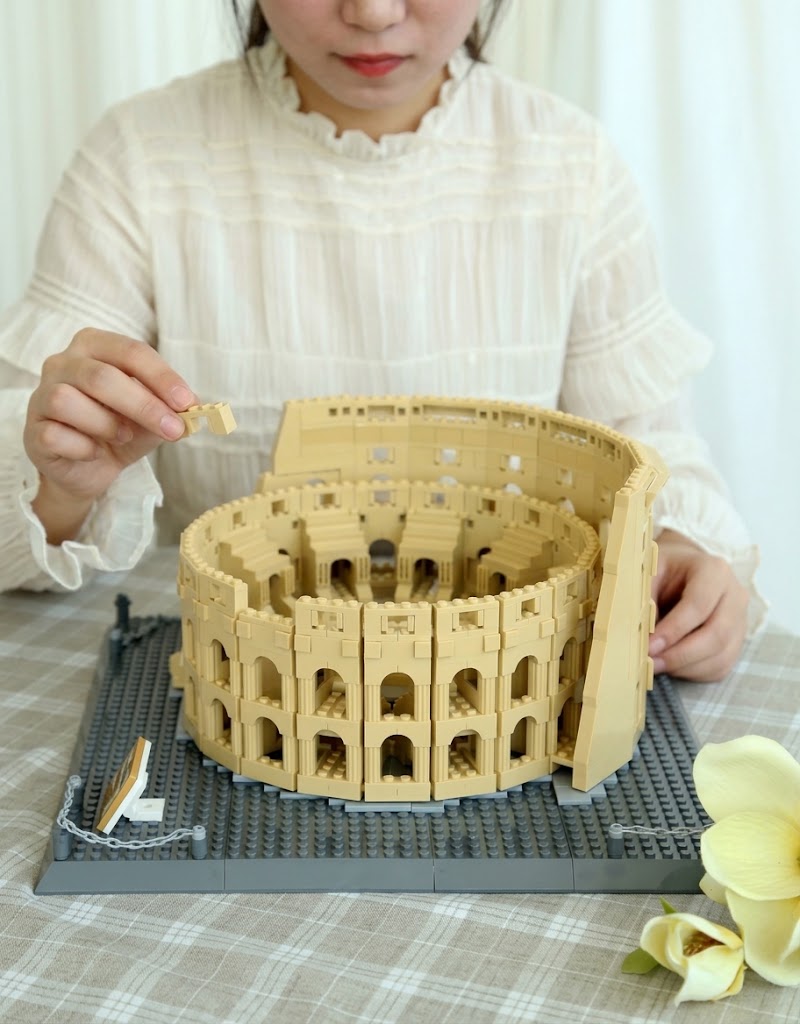 Hands assembling the 1953-piece miniature Roman Colosseum architecture building block model on a table.