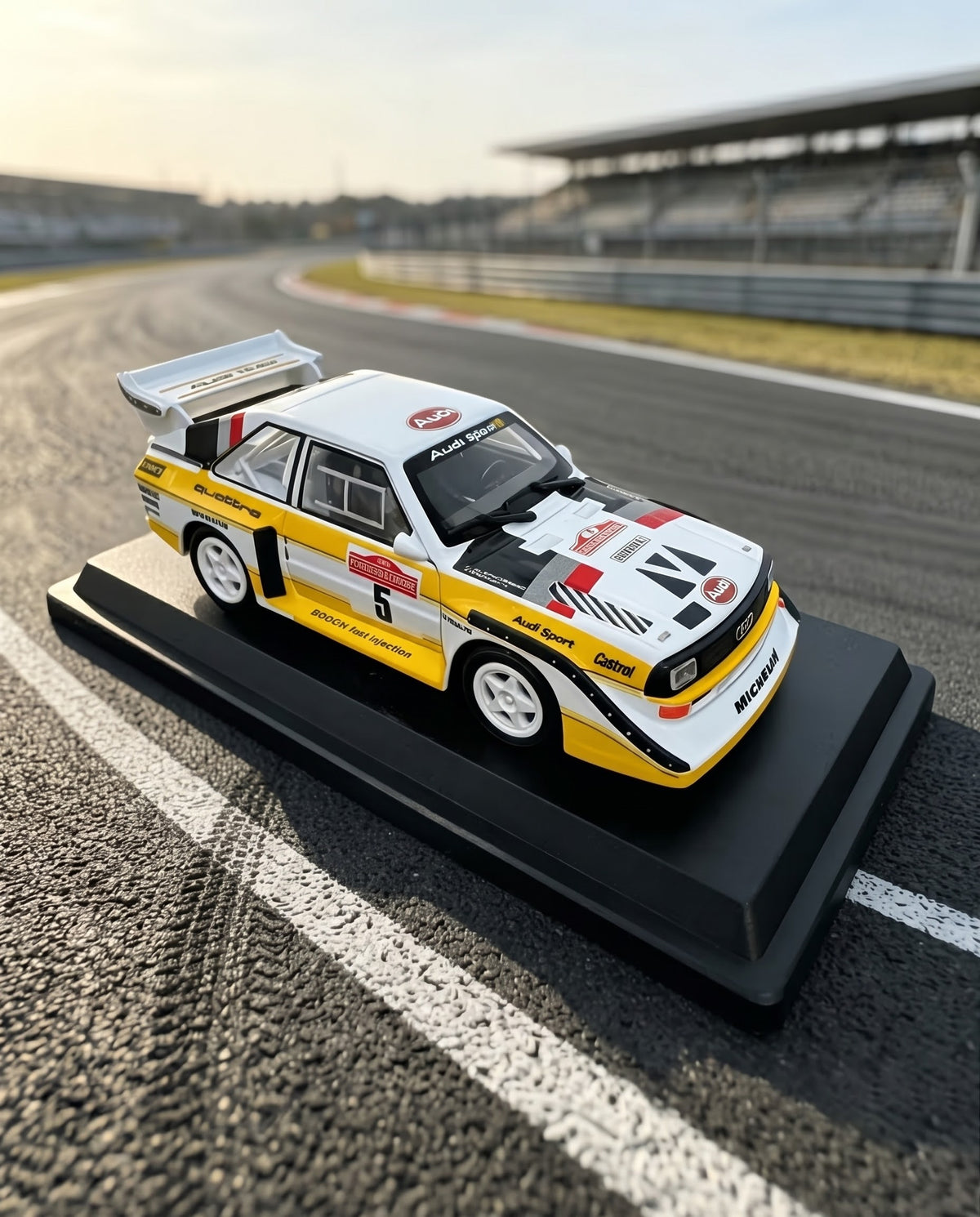 Front three-quarter view of the 1985 Audi Sport quattro S1 E2 Group B rally diecast car by Bburago on an asphalt circuit racetrack.