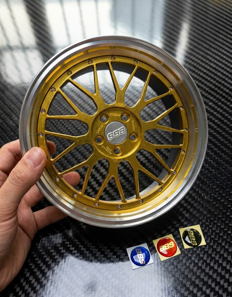 Gold 10cm BBS style mesh wheel model held in hand showing scale alongside blue red and black center cap stickers
