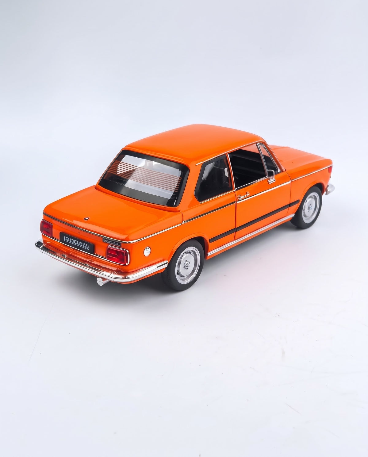 High-angle rear view of the orange 1/18 BMW 2002 tii diecast car highlighting classic rectangular taillights, chrome bumper, chrome exhaust tip, and rear window defroster lines.
