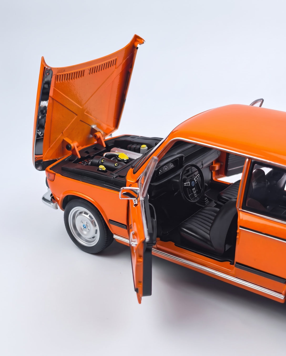 Detailed close-up of the 1/18 BMW 2002 tii diecast car showing open forward-hinged bonnet, replica fuel-injected engine compartment, dashboard gauges, and textured interior.