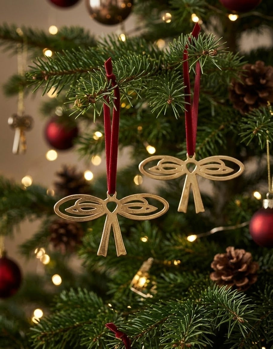 Vintage-inspired gold metal ribbon bow ornaments with red velvet straps hanging on a lit Christmas tree.