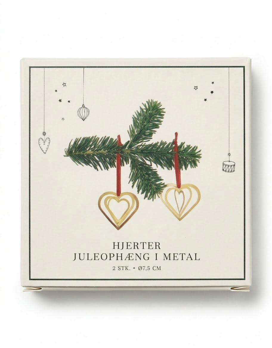 Two Scandinavian layered gold metal heart Christmas ornaments with red hanging loops inside cream gift box.