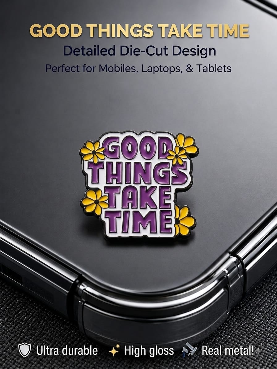 "Good Things Take Time" die-cut metal enamel sticker with purple typography and yellow flowers applied to the back of a black smartphone.