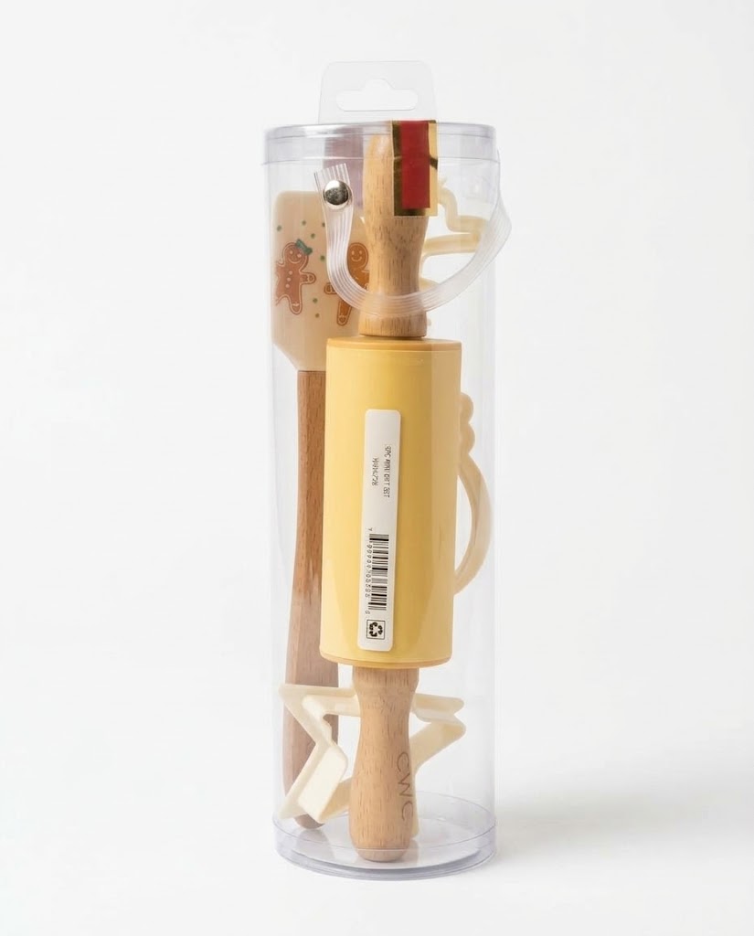 Pastel yellow holiday baking kit inside gift tube with gingerbread man silicone spatula, mini wooden rolling pin, and star cookie cutter.