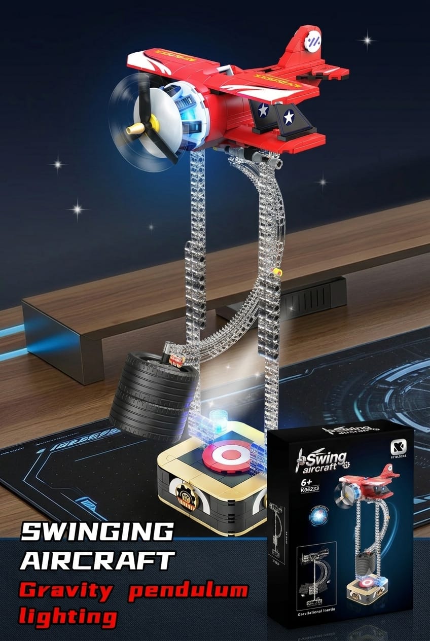 Red kinetic swing aircraft toy balancing on a computer desk setup next to product packaging with illuminated base lights.