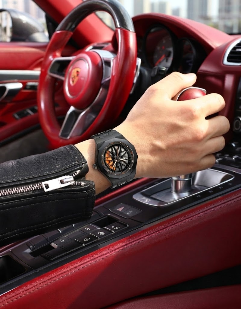 Driver wearing a black automotive rotating wheel rim wristwatch on stainless steel bracelet while shifting gears.