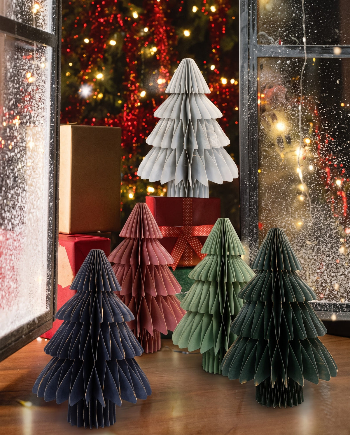 Assorted 3D honeycomb paper Christmas trees in festive colors displayed with gift boxes by a snowy winter window, available in Lebanon.