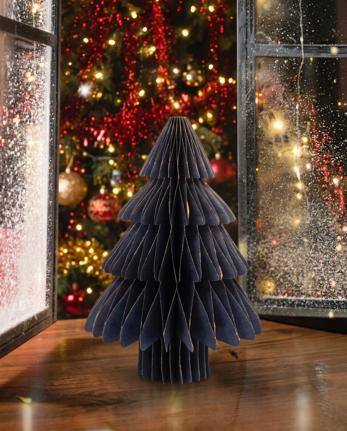 Modern midnight navy blue pleated paper tabletop Christmas tree with metallic gold edges beside cozy holiday window lights in Lebanon.