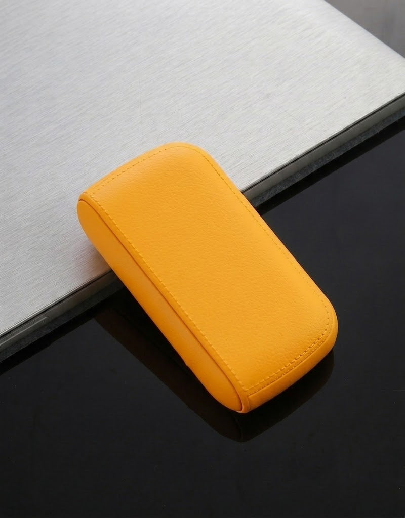 Warm yellow waterproof leather cigarette case with perimeter stitching and lock closure displayed on a modern desk.
