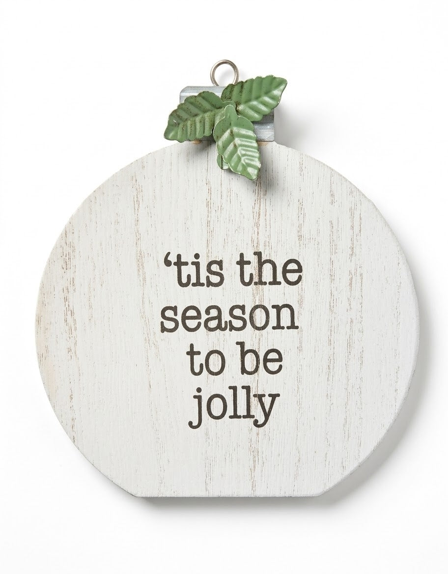 Distressed white wooden Christmas bauble sign featuring the quote "'tis the season to be jolly" with embossed green metal holly leaves and hanging loop on a plain white studio background.